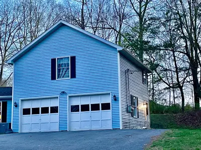 a blue house with two white garage doors at Walk to the Outfield of Lime Rock Park in Salisbury