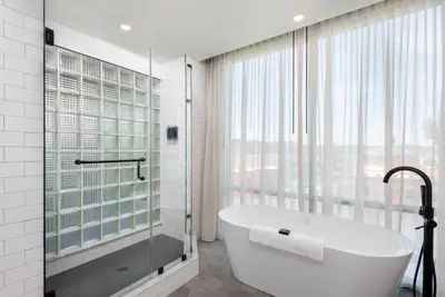 a bathroom with a tub and a shower and a window at voco James Newbury Hudson Valley by IHG in Coxsackie