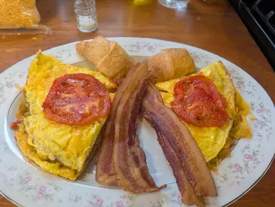 a plate of breakfast food with bacon and eggs at The White House Inn in Cooperstown