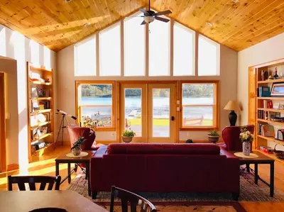 a living room with a red couch and a large window at Silver Lake Cabin w/ Own Lake! (near Cooperstown) in New Berlin