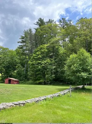 a field with a stone wall and a barn and trees at The Tannery House in Claryville