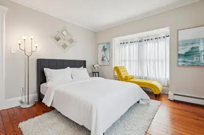 a white bedroom with a bed and a yellow chair at Grace's Place - 3 Bedroom Townhouse in Greenwich in Greenwich