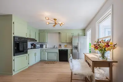 a kitchen with green cabinets and a table with a vase of flowers at Fairfield Cottage -Top Rated Gem, Fire Pit, Near Beach, 90 Min to NYC in Fairfield