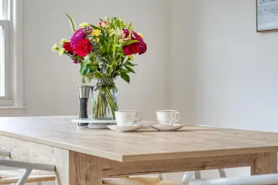 a table with two cups and a vase with flowers at Fairfield Cottage -Top Rated Gem, Fire Pit, Near Beach, 90 Min to NYC in Fairfield