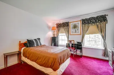 a bedroom with a bed and a desk and two windows at Woodsy Ballston Spa Home 4 Mi to State Park! in Ballston Spa