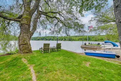 a tree with two chairs and a boat on the water at Lakefront Westhampton Cabin with Beach and Kayaks! in Westhampton