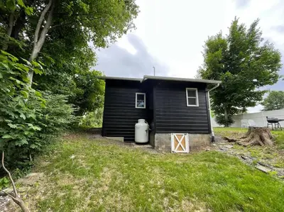 a small black house with a garbage can in a yard at Campfire Cottage Fireplace, fire pit & no chores! in Kingston