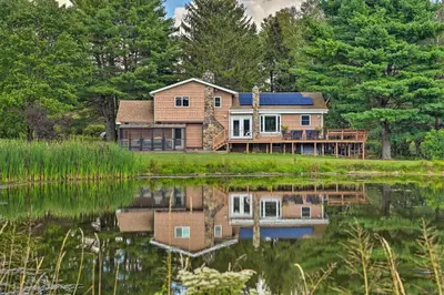 a house on a hill with a reflection in the water at Catskills Farmhouse and Spa in Harpersfield