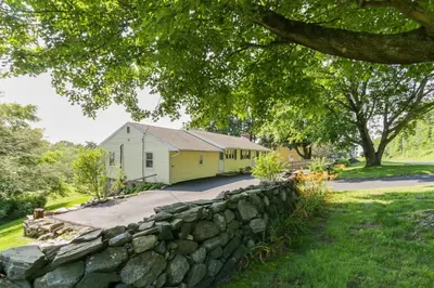 a stone wall in front of a yellow house at Connecticut Retreat Steps to Historic Downtown! in Litchfield