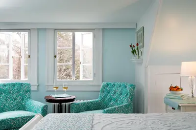a bedroom with two chairs and a bed and two windows at Four Chimneys Inn in Bennington
