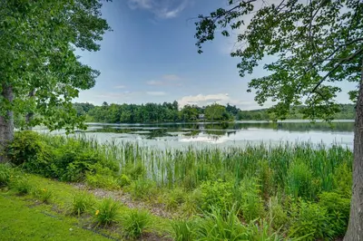 a view of a lake from between two trees at Lakefront West Sand Lake Home with Beach Access! in West Sand Lake