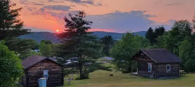 two old buildings in a field with the sunset in the background at Lake Lauderdale Campground in Cambridge