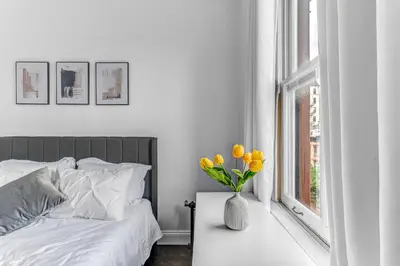 a white bedroom with a bed and a vase of yellow tulips at 2Bd Stylish Brooklyn Heights - Steps WaterFront in Brooklyn