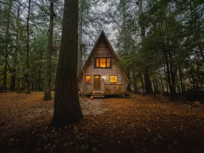 a small cabin in the woods with its lights on at Enchanting River- Water Front A-Frame Cabin in Yulan