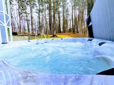 a jacuzzi tub with snow and trees in the background at The Athena Hideaway - hottub, firepit, lake & racetrack in Saratoga Springs