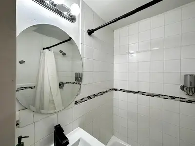 a white tiled bathroom with a sink and a mirror at 1-A Diamond in Yonkers, NY in Yonkers