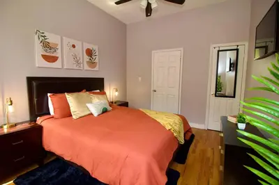 a bedroom with a bed with an orange bedspread at Tuk Ahoy - Sunset Suite 2B with Shared Spaces in Brooklyn