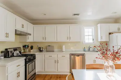 a white kitchen with white cabinets and a table at Urban Downtown Stamford Home 45 min to NYC with Garage And Yard in Stamford