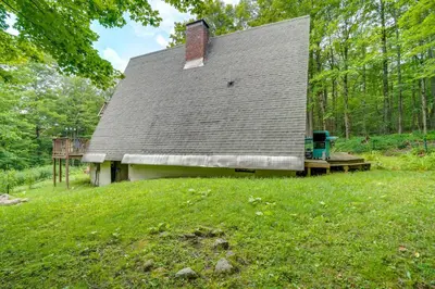 a house in the middle of a grassy field at A-Frame Cabin with Furnished Deck in Becket! in Becket