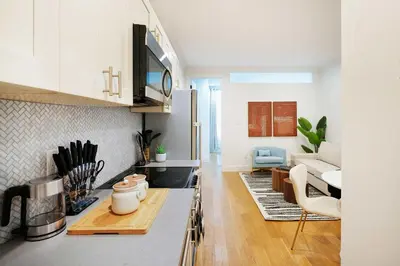 a kitchen with white cabinets and a living room at 1290-7 New Renovated 2 Bedrooms in UES in New York