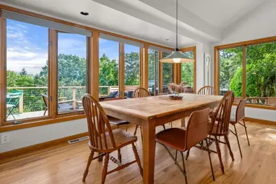 a dining room with a wooden table and chairs and large windows at Relaxing Catskill Escape- Mountain Views - Hot Tub - Fire Pit - Heated Pool in Catskill