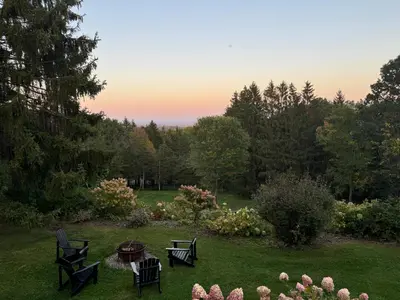 a backyard with a table and chairs in the grass at Relaxing Catskill Escape- Mountain Views - Hot Tub - Fire Pit - Heated Pool in Catskill