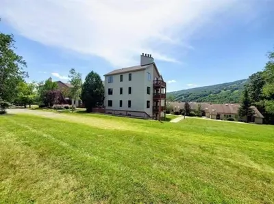 a large grassy field in front of a white house at Mt Snow Condo with Pool Mountain Views Half Mile to Mtn in Dover