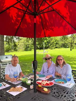 three people sitting at a table under an umbrella at French Woods Farmhouse Bed & Breakfast in Hancock