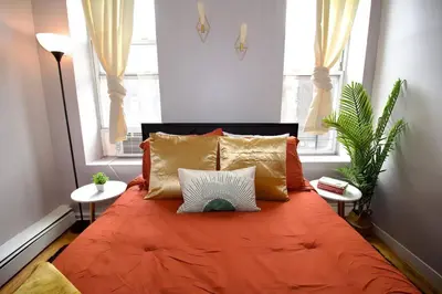 a bedroom with an orange bed with two windows at Tuk Ahoy - Sunset Suite (3B) with Shared Spaces in Brooklyn