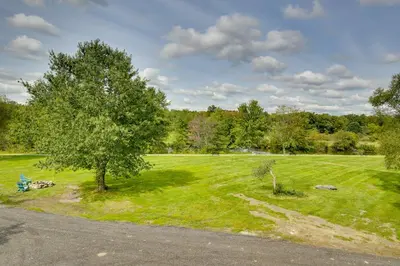 a green field with a tree and a bench at Fire Pit and On-Site Pond Hudson Valley Home! in Wappingers Falls