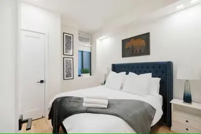 a white bedroom with a large bed with a blue headboard at Luxury 2BR Duplex 5min to Central Park in New York