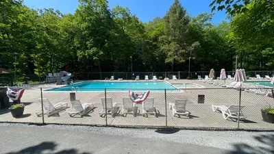 a fence with chairs and a swimming pool at Cozy Cabin at Poconos With Hot Tub and Fire Pit in East Stroudsburg