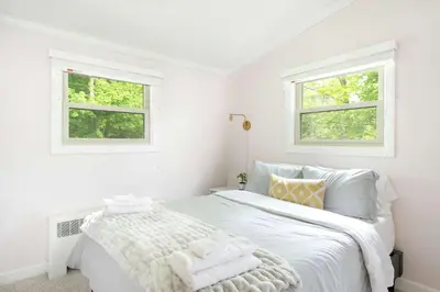 a white bedroom with a bed with two windows at Berkshire Vacation Rentals: Great Barrington Walkable To Lake And Town in Great Barrington
