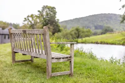 a wooden bench sitting in the grass next to a lake at Berkshire Vacation Rentals: The Brookman: Renovated 6000 SF Estate On 40 Acres in Williamstown