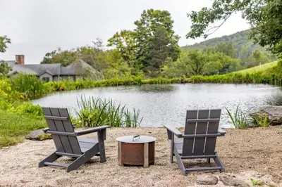 two chairs and a table in front of a lake at Berkshire Vacation Rentals: The Brookman: Renovated 6000 SF Estate On 40 Acres in Williamstown