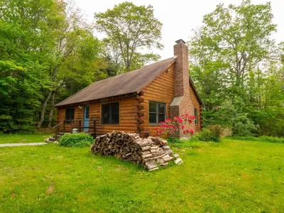a log cabin with a pile of logs in front of it at Berkshire Vacation Rentals: Private Cabin On Over 12 Acres Of Woods in Becket