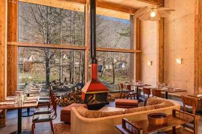 a living room with a fireplace and a large window at Eastwind Hotel Oliverea Valley in Big Indian
