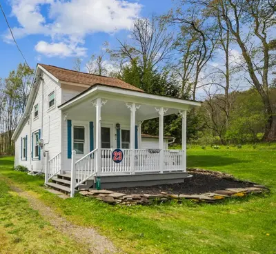 a white house with a porch on a grass field at Cozy Milford Cottage on Half Acre w Deck & Grill in Milford