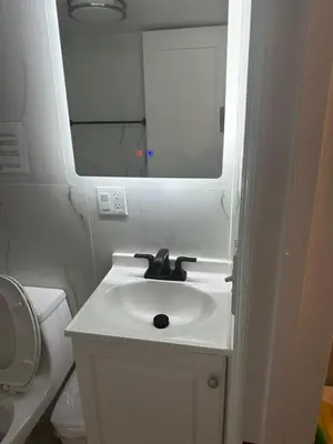 a white bathroom with a sink and a mirror at Cozy Apartments Woodside near Manhattan in Queens