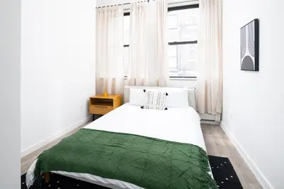 a bedroom with a white bed with a green blanket at Spacious Luxury 2BD Downtown Gym W/D Doorman in New York