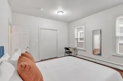 a white bedroom with a bed and a chair at Frog Hollow Red Door Loft in Hartford