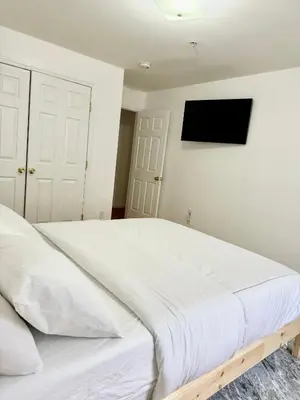 a white bed in a bedroom with a tv on the wall at Stylish Evergreen Apartment By Newark Airport in Newark