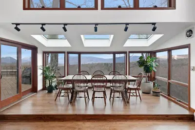 a dining room with a table and chairs and windows at 5 Star Gorgeous Cliffside Chalet with Panoramic Views in Tannersville