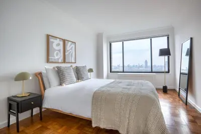 a white bedroom with a large bed and a large window at Blueground UES gym balcony nr central park NYC-1404 in New York