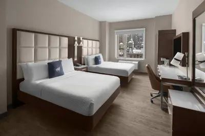 a hotel room with two beds and a desk at Cambria Hotel New York - Chelsea in New York