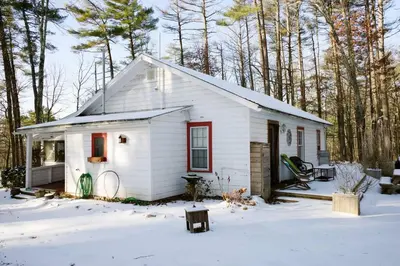a small white house with red windows in the snow at Enchanted Woodstock Cottage with hot tub in West Hurley