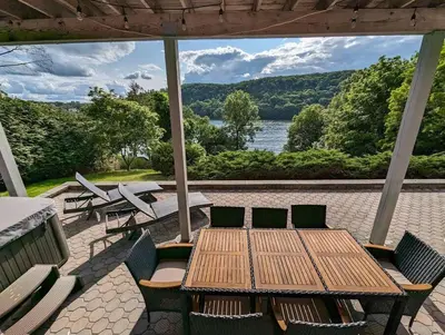 a patio with a wooden table and chairs and a lake at Candlewood Lake -Family Getaway, Lakefront 3775 sqft Home in Danbury