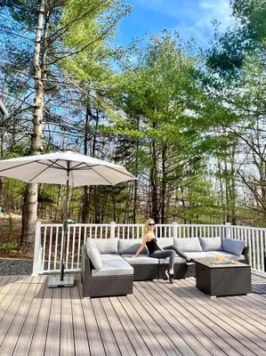 a woman sitting on a couch on a deck with an umbrella at Brand New House with Huge Patio in Kerhonkson