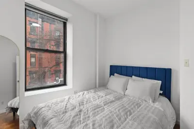 a bedroom with a bed with a blue headboard and a window at 89-3FS Newly Furnished 2br 1bath UES in New York