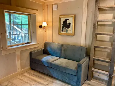 a couch in a living room with a window and a window at Little Birds Treehouse in Sparrow Bush